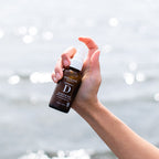 A hand holding a small amber spray bottle of botanical D moisture mist