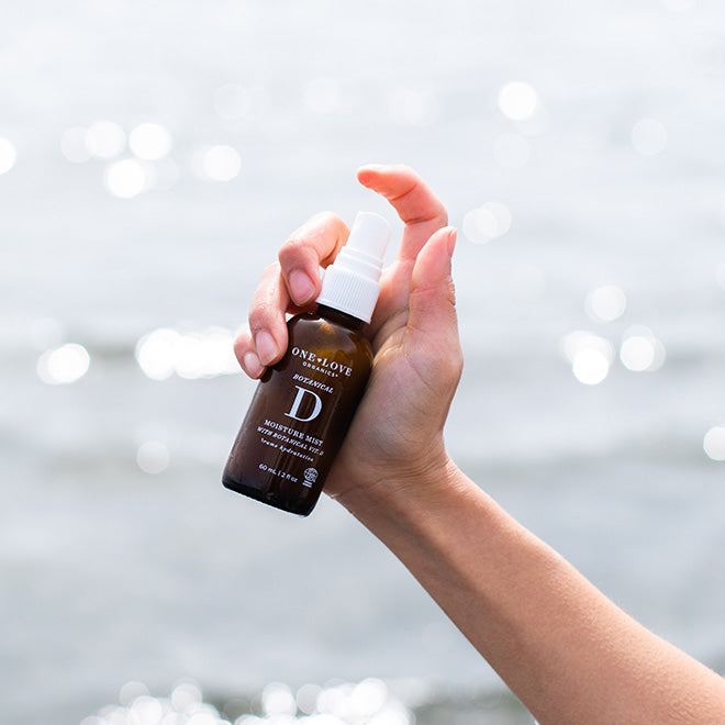 A hand holding a small amber spray bottle of botanical D moisture mist