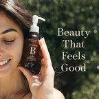A woman outdoors holds a bottle of One Love Beauty Botanical Enzyme Cleansing Oil 