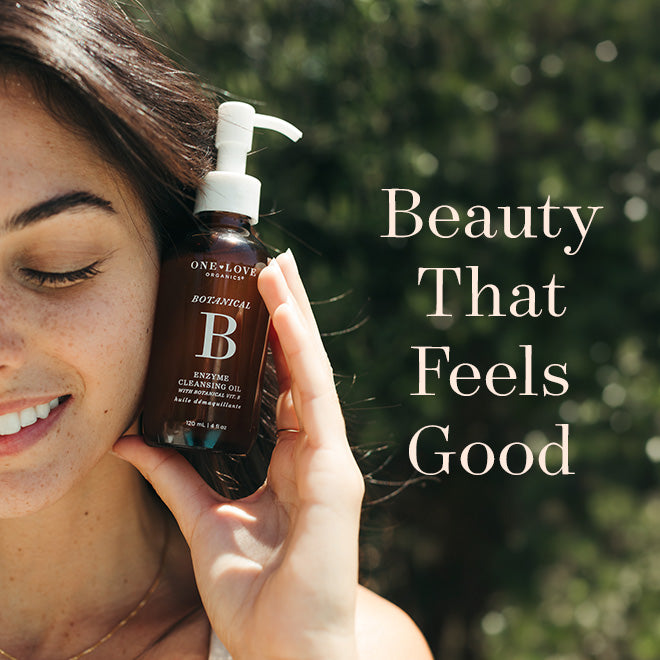 A woman outdoors holds a bottle of One Love Beauty Botanical Enzyme Cleansing Oil 