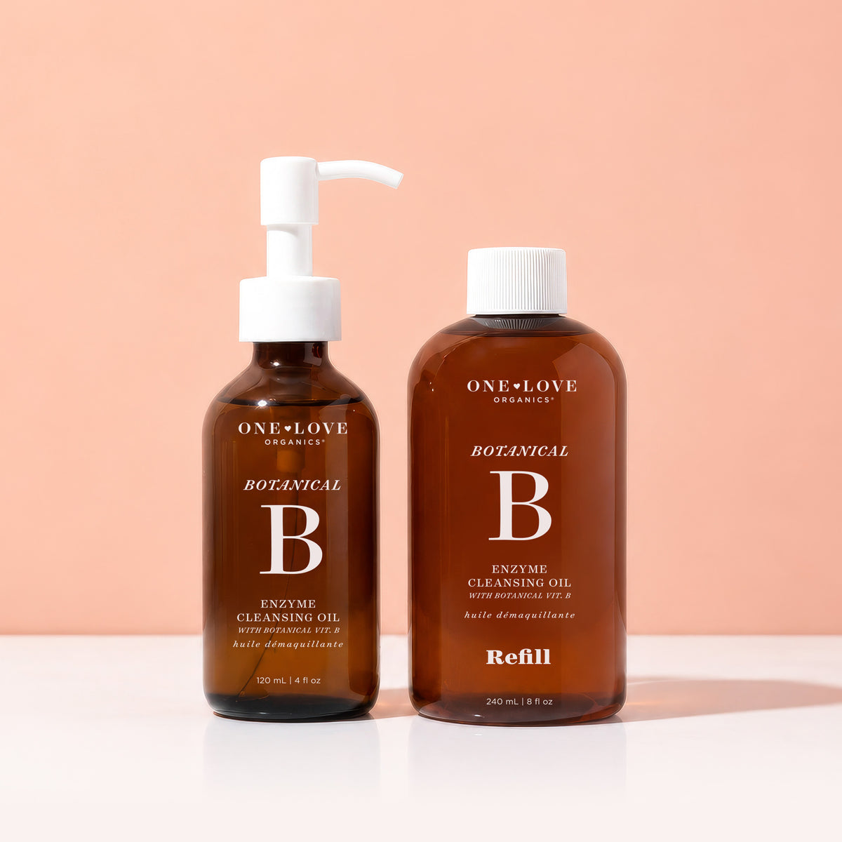 Two bottles of One Love Organics Botanical Enzyme Cleansing Oil on a peach background