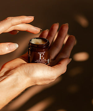 A close-up of hands holding an open botanical e eye cream 