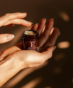 A close-up of hands holding an open amber cosmetic jar with a white cream visible at the top.
