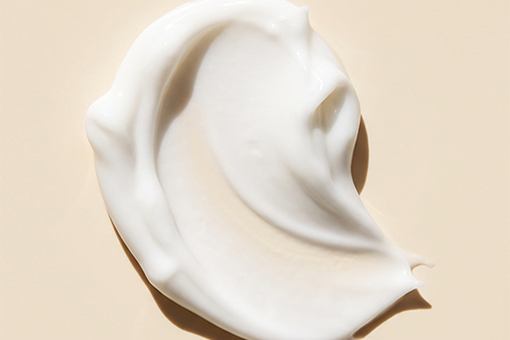 A thick, creamy white cosmetic swirled in a smooth, curved shape on a warm beige background.