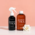 Two bottles of One Love Organics gardenia tea products on a peach background with a white flower.