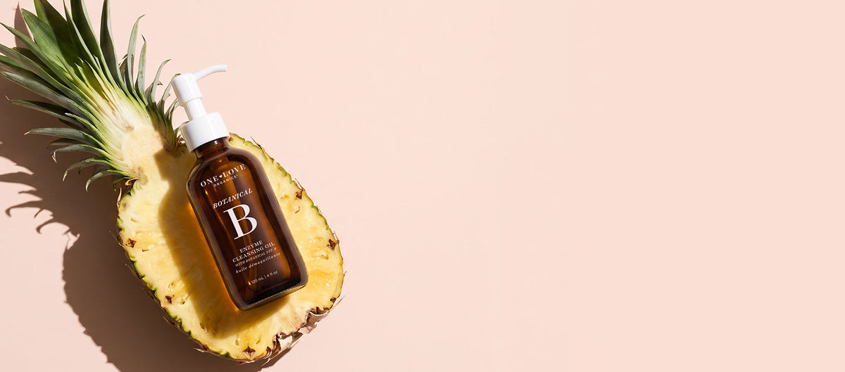 A brown pump bottle labeled botanical b by One Love Organics, placed on a sliced pineapple.