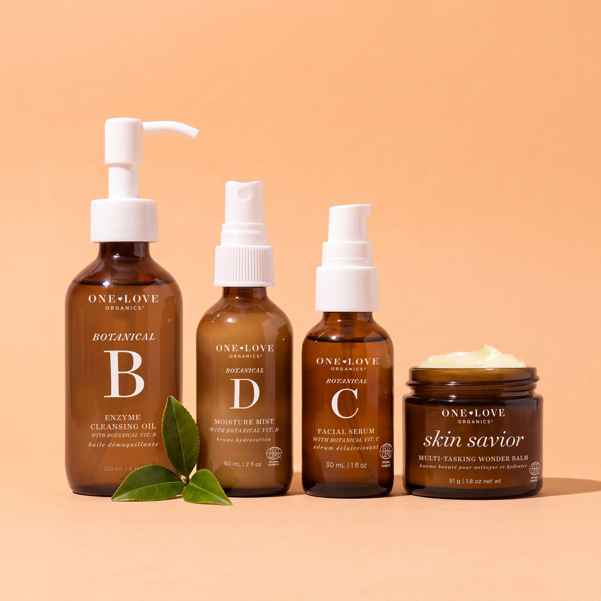 Four One-Love Organics botanical hair and skin care products arranged on a peach studio background
