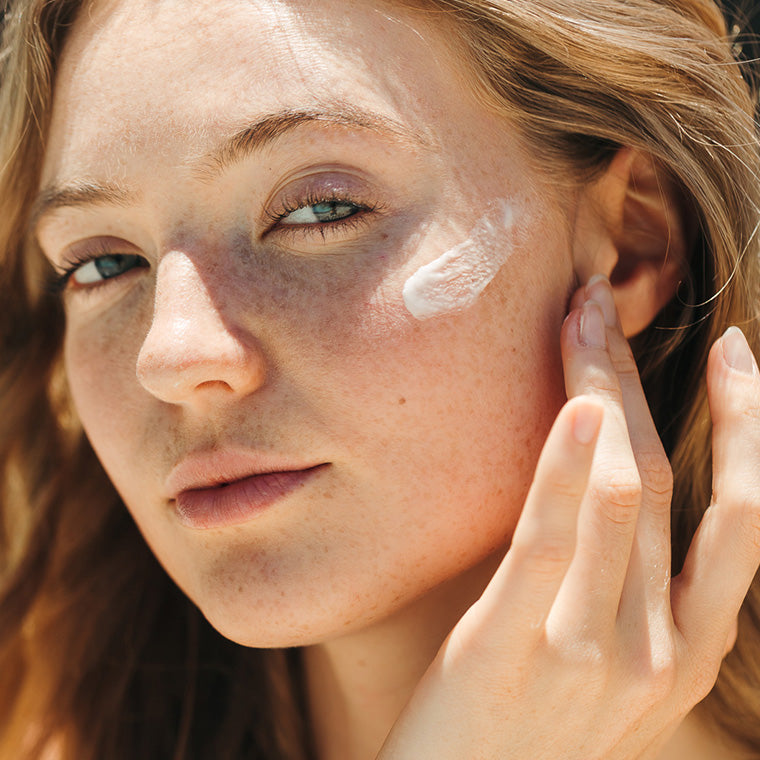 Close-up of a woman outdoors with white sunscreen cream applied to her cheek and being touched by her finger.