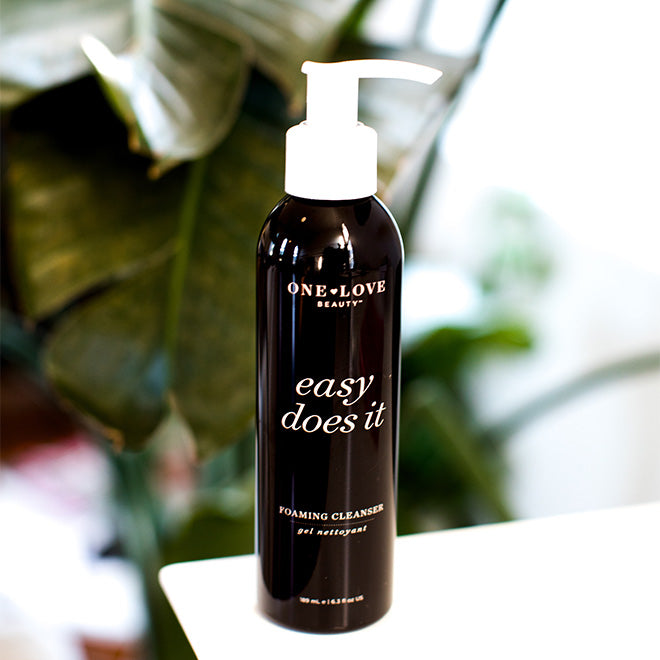 A bottle of One Love Beauty Easy Does It Foaming Cleanser with a white pump dispenser on a white surface