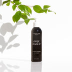 A bottle of One Love Beauty Easy Does It Cleansing Cleaner, standing on a reflective white surface 