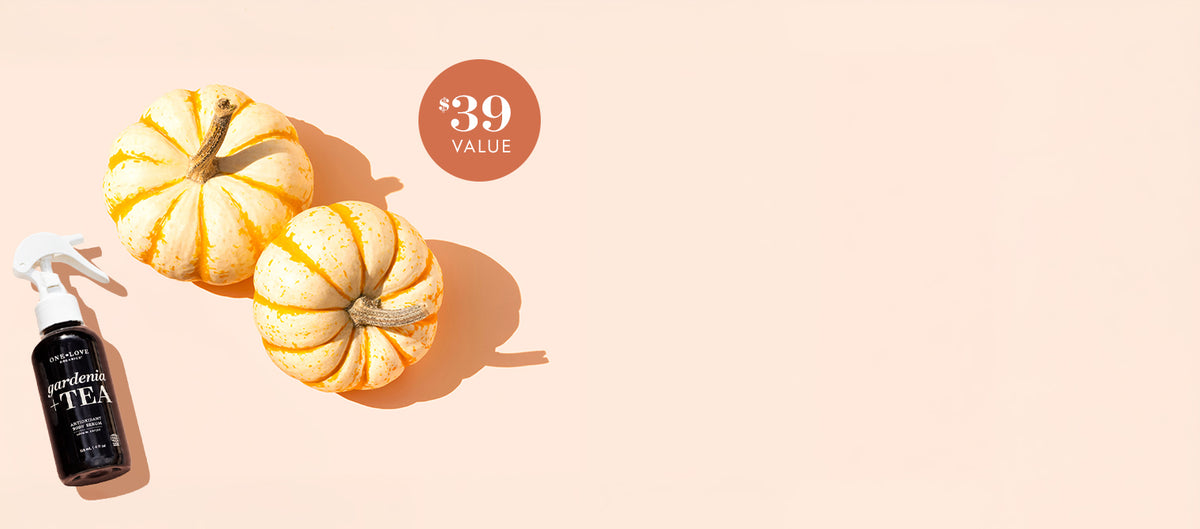 A small black spray bottle labeled 'Gardenia + Tea' styled on a warm peach background