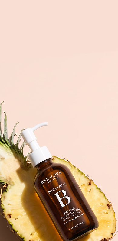 Bottle of BOTANICAL B Enzyme Cleansing Oil styled on a sliced pineapple half.