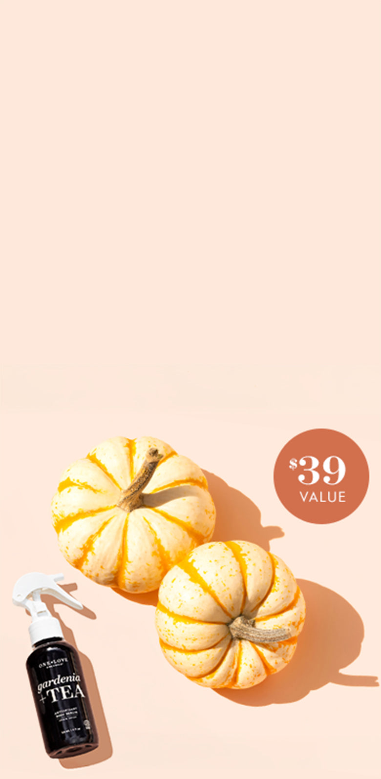 A black spray bottle labeled 'Gardenia TEA' styled with two small striped orange and cream pumpkins.