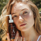 A close-up lifestyle shot of a woman with holding a bottle of One Love Botanical A Facial Cleansing Oil. 
