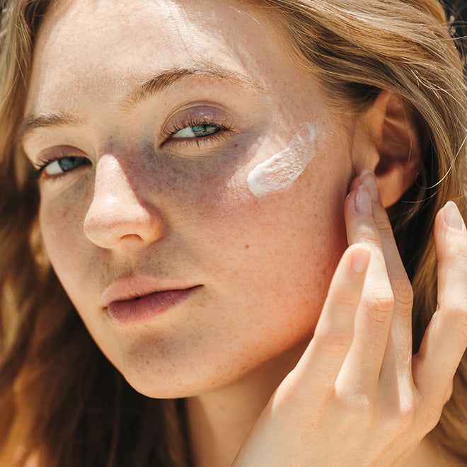 Close-up of a woman outdoors with white cream applied to her cheek