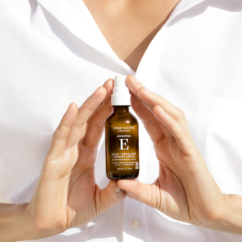 A person in a white collared shirt holds a bottle of botanical e firming cream