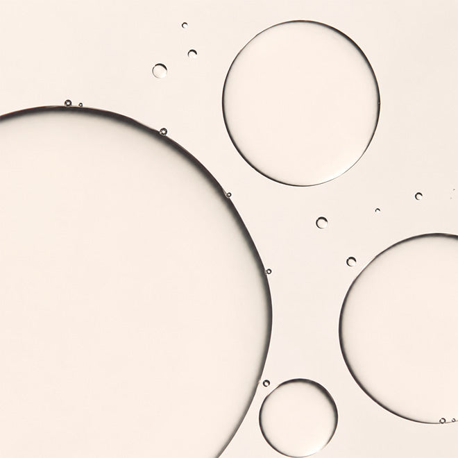 Abstract close-up of translucent circular droplets and large liquid bubbles on a warm off-white background.