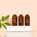Three bottles of One Love Organics Botanical D Moisture Mist arranged on a white surface with a plant and a pink crystal in the background.